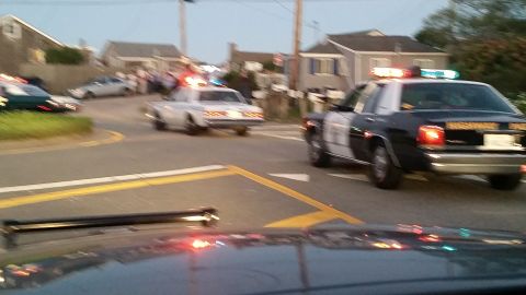 1991 Ford LTD Crown Victoria - Photo of a Highway Patrol cruiser and other police cars with emergency lights at a seaside intersection at dusk.