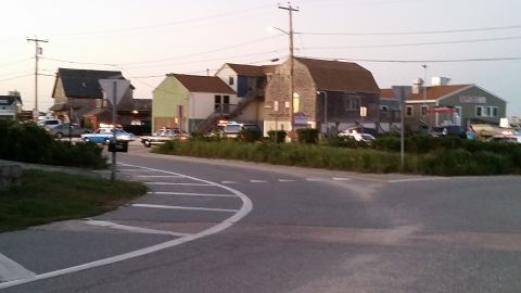 1991 Ford LTD Crown Victoria - Photo of a coastal village intersection with shingled buildings and parked cars at dusk.