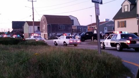 1991 Ford LTD Crown Victoria - Photo of several police cruisers with emergency lights spread across a seaside intersection at dusk.