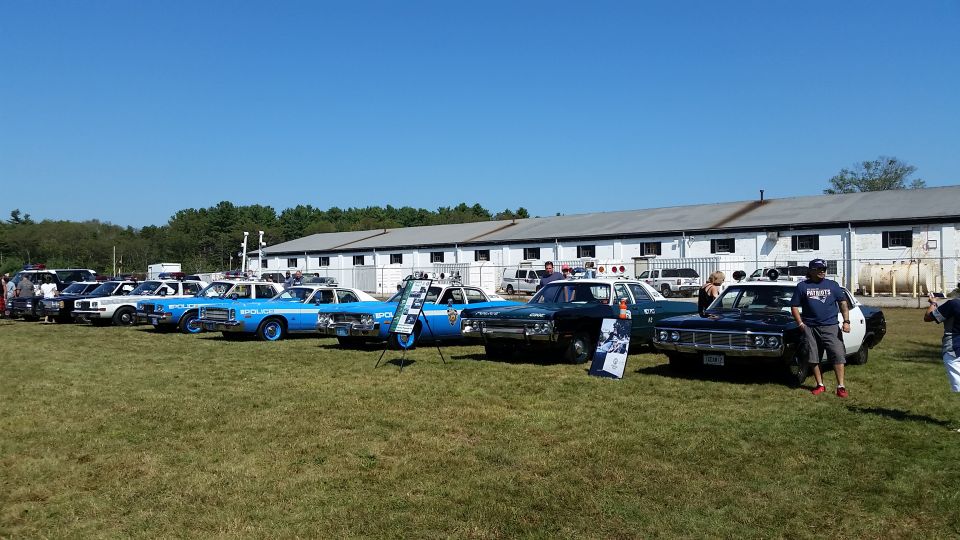 Vintage police cars parked in a line on grass in front of a white building.