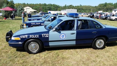 1991 Ford LTD Crown Victoria - A dark blue and light blue two-tone 1991 Ford Crown Victoria police car is parked on a grassy field with other vehicles in the background.