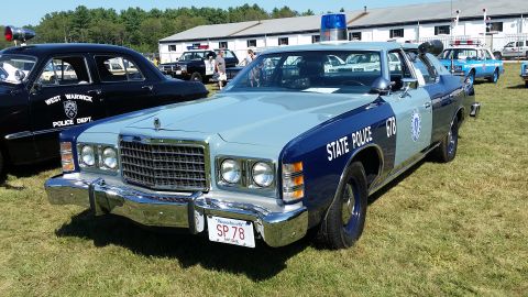 1991 Ford LTD Crown Victoria - A light blue and dark blue 1970s era police car is parked on a grassy field with a building in the background. The car has "STATE POLICE 67…