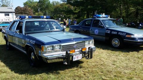 1991 Ford LTD Crown Victoria - Two Ford Crown Victoria police cars are parked on a grassy field on a sunny day. The car in the foreground has "90E STATE POLICE" written o…