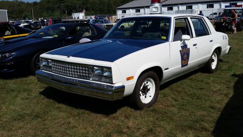 1991 Ford LTD Crown Victoria - A white and blue 1980s era Pennsylvania State Police sedan is parked on a grassy field next to other vehicles. The car features a light bar…