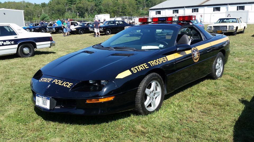 Black 1990s Chevrolet Camaro Z28 convertible state police car with yellow decals and light bar.