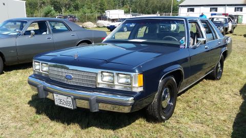 1991 Ford LTD Crown Victoria - A dark blue 1991 Ford Crown Victoria sedan is parked on a grassy area with trees and buildings in the background. The front of the car is a…