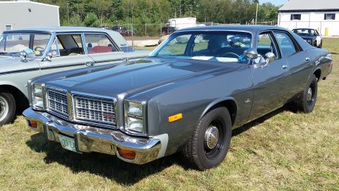 1991 Ford LTD Crown Victoria - A dark gray 1970s era Dodge sedan is parked on a grassy field with another classic car to its left. The car features a chrome grille and bu…