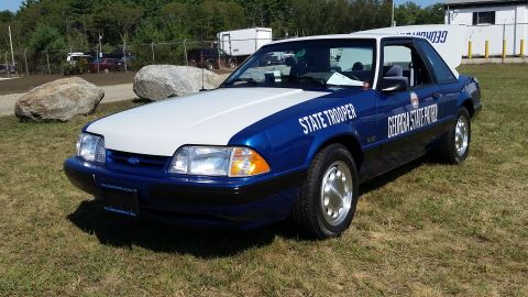 1991 Ford LTD Crown Victoria - A blue and white 1991 Ford Mustang LX convertible, marked as "STATE TROOPER" and "GEORGIA STATE PATROL", is parked on a grassy area with tr…