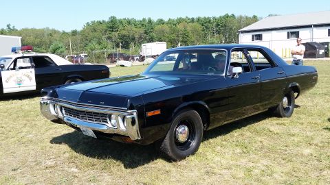 1991 Ford LTD Crown Victoria - A black 1974 Dodge Polara police car is parked on a grassy field next to another police vehicle.
