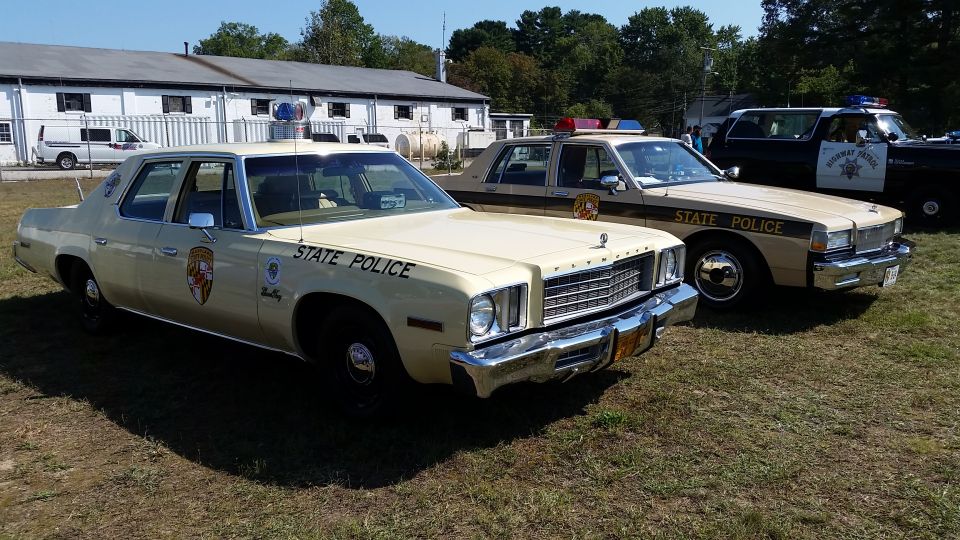 Cream-colored 1977 Plymouth Fury police car with "STATE POLICE" text, parked on grass