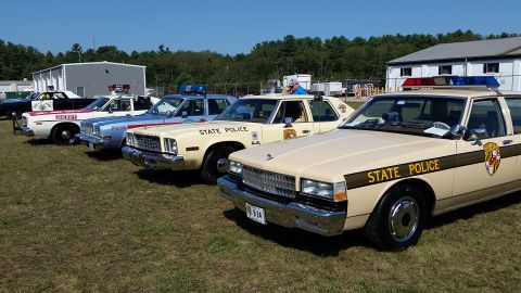 1991 Ford LTD Crown Victoria - A line of vintage state police vehicles are displayed outdoors on a sunny day.