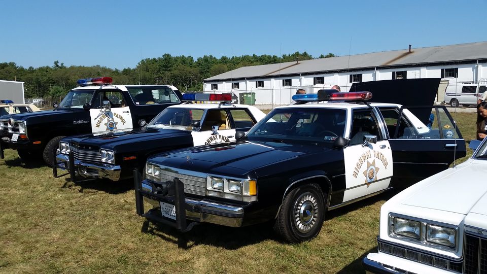 Several highway patrol cars parked on grass, one with hood and door open
