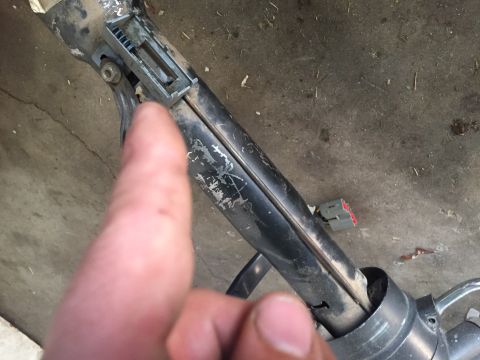 1986 Ford Bronco - A close-up view of a vehicle's steering column component, with a finger indicating a specific area.