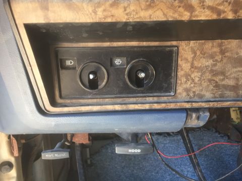 1986 Ford Bronco - Close-up of the interior dashboard, headlight and wiper controls, wood grain accents, and the brake release lever.