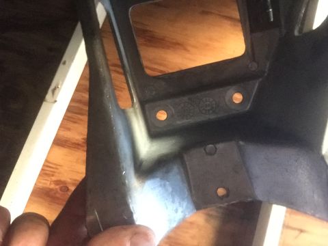 1986 Ford Bronco - A black plastic part with visible screw holes and circular indentations is held by a hand.