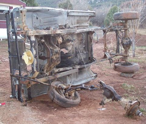 1990 Ford Bronco - Vehicle chassis overturned in a yard, showing extensive rust and damage.