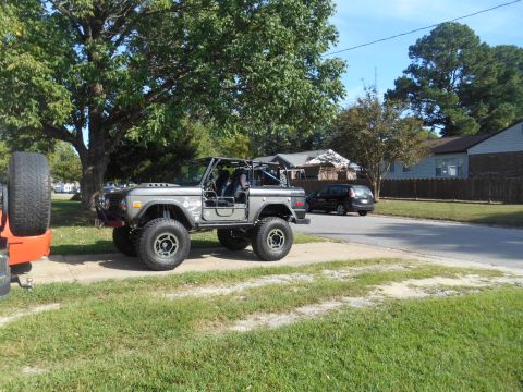 1972 Ford Bronco - A modified gray Ford Bronco is parked on a residential street next to a black minivan.