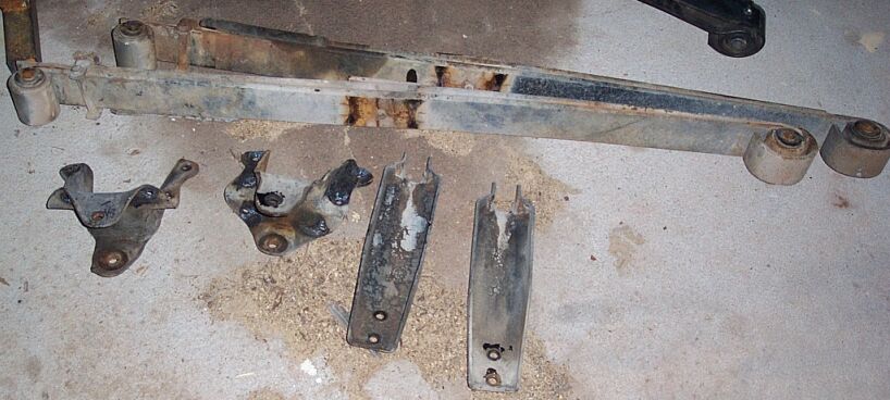 Removed radius arm with white poly bushings and four cut-off suspension brackets on a shop floor