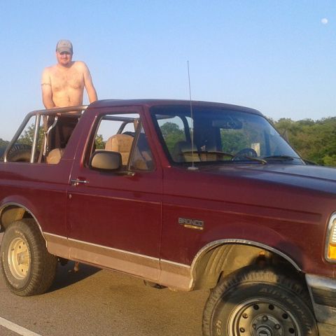 1996 Ford Bronco - A man stands in the open roof of a maroon 1996 Ford Bronco.