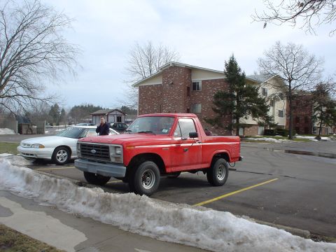 1980 Ford Bronco - A red Ford Bronco is parked in a lot next to a white sedan with snow on the ground.