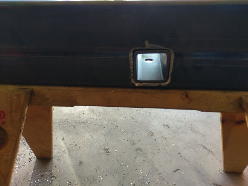 Metal tube with a square cut-out, supported by wooden sawhorses