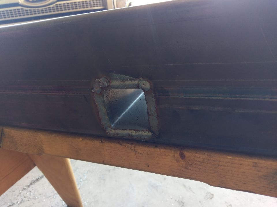 welded square hole in dark metal tube, resting on wood