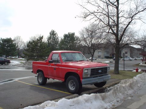 1980 Ford Bronco - This red pickup truck, likely from the early 1980s, is parked in a lot with snow on the ground.