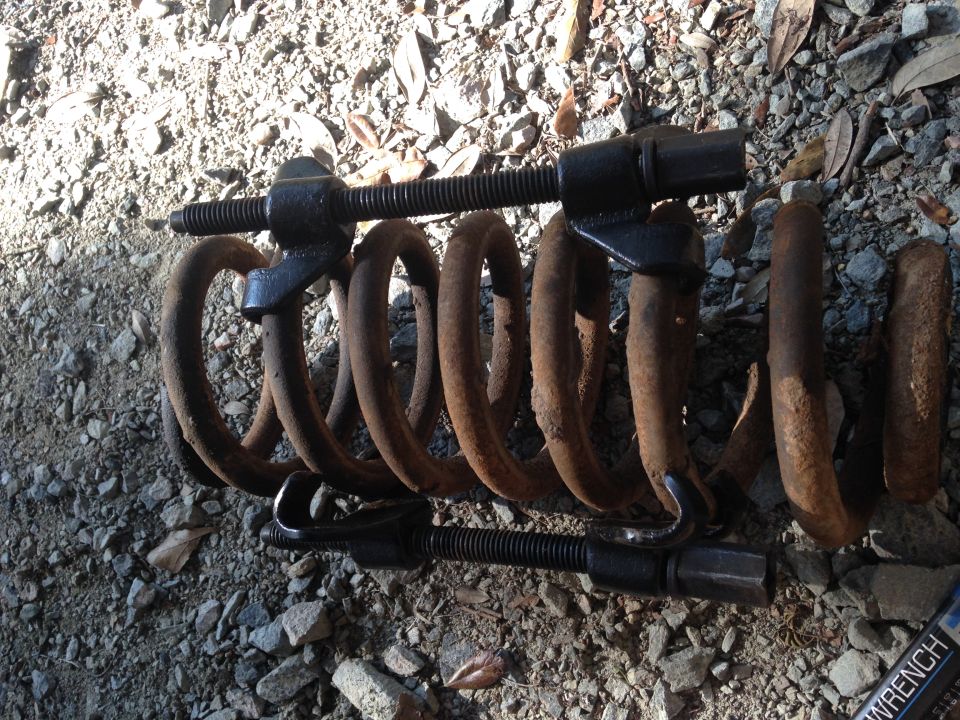 Rusty coil spring with a black spring compressor tool on a gravel surface