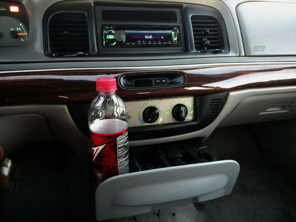 1995 Mercury Grand Marquis interior dashboard with wood trim, aftermarket stereo, and a bottle of soda