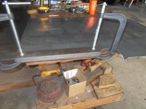 1992 Ford Bronco - A metal sheet is secured with clamps on a workbench, alongside tools and automotive parts.