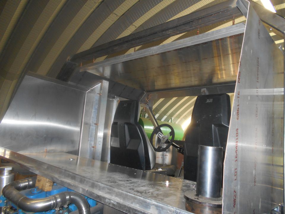 Interior view of a custom vehicle build, showing unfinished metalwork, two bucket seats, and a steering wheel