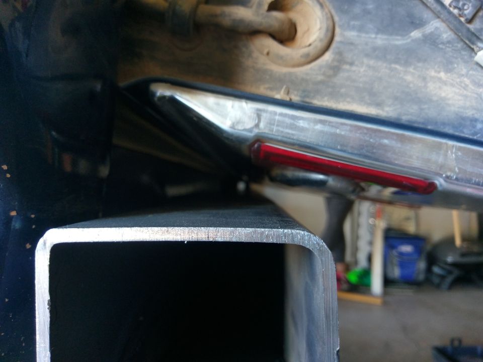 Close-up of a trailer hitch receiver in front of a vehicle's rear bumper with a red reflector