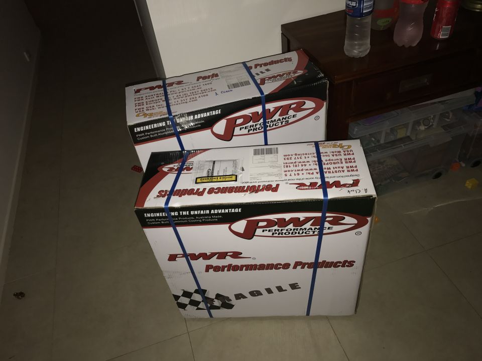Two PWR Performance Products shipping boxes with blue straps on a tiled indoor floor