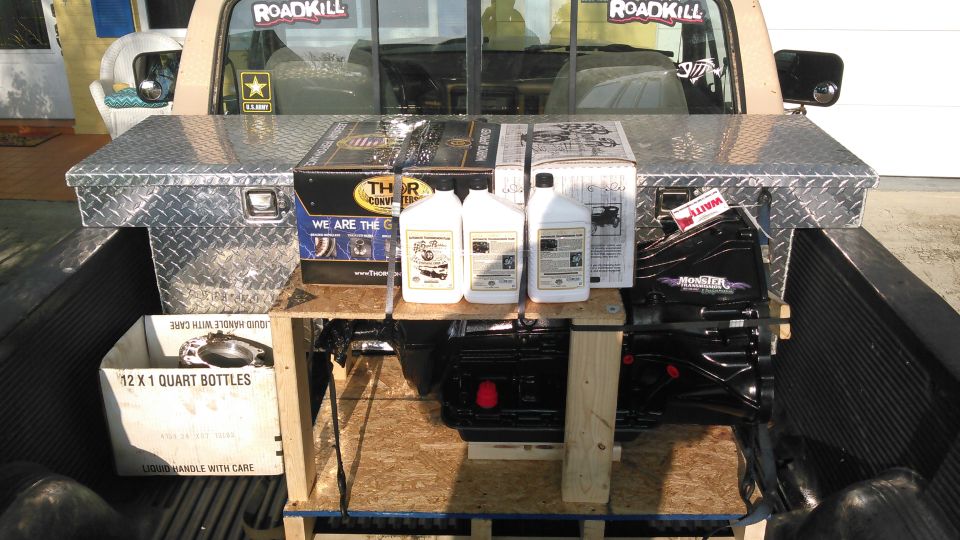 Pickup truck bed loaded with oil bottles, parts boxes and a transmission on a crate
