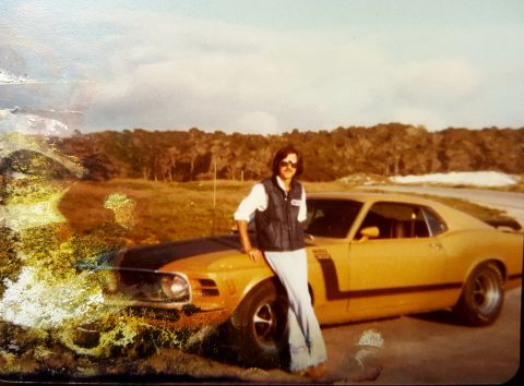 1973 Ford Mustang - A man poses with a yellow 1970 Boss 302 Mustang, identifiable by its distinctive body style and racing stripes.