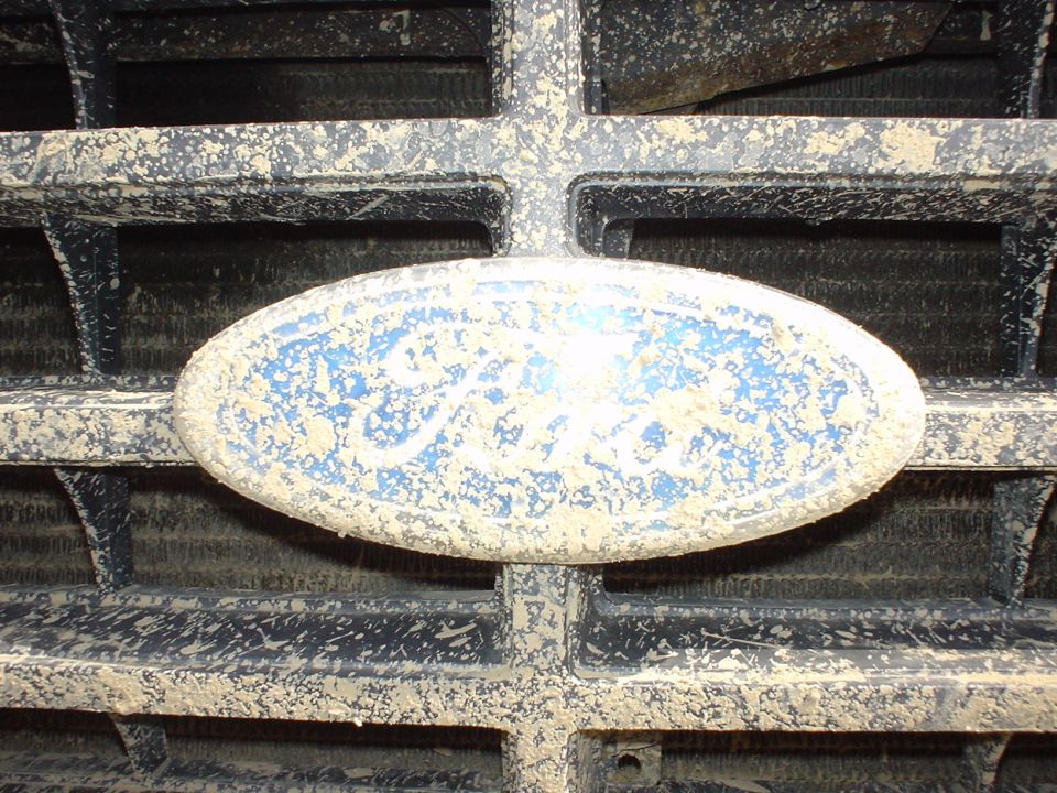 Ford emblem on a dirty grille. Supermotors.net logo at bottom right