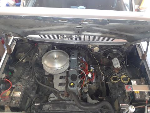 1985 Ford Bronco - The engine bay of a vehicle, a V8 engine, air filter, and battery, with visible wiring and hoses.