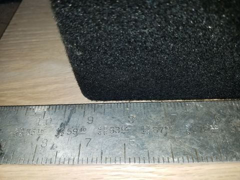 1994 Ford Bronco - A close-up view of a black carpeted object being measured with a metal ruler, indicating its dimensions.