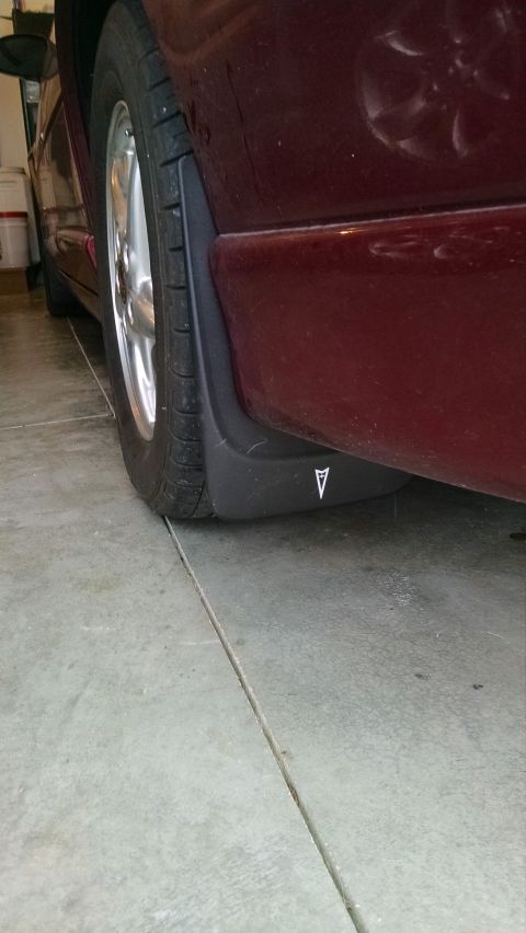 2002 Pontiac Grand Prix - Close-up of a black Pontiac mud flap bearing the arrowhead logo on the lower rocker of a dark red vehicle in a garage.