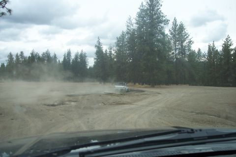 1995 Ford Bronco - SUV driving on a dirt road, kicking up dust clouds near a forest.