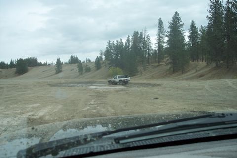 1995 Ford Bronco - A white 1995 Ford Bronco navigates a muddy off-road course under an overcast sky.
