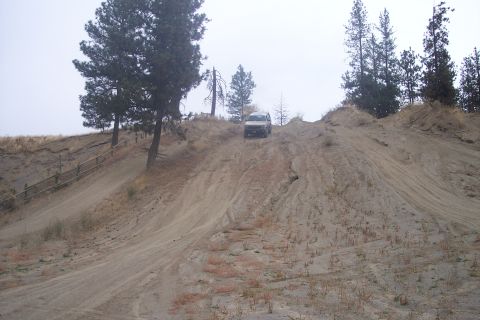 1995 Ford Bronco - A white 1995 Ford Bronco navigates a steep, sandy incline in an off-road environment.
