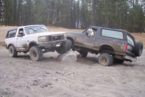 1995 Ford Bronco - Two Ford Broncos navigate a rocky off-road course, with one vehicle perched on a large boulder.