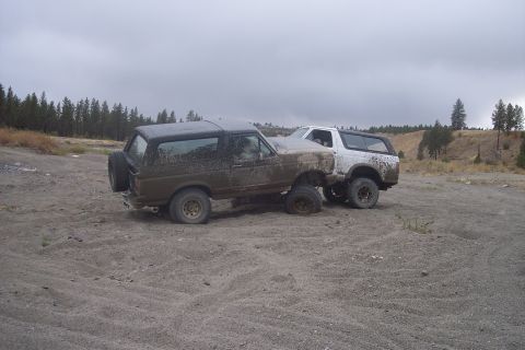 1995 Ford Bronco - Two Ford Broncos are parked on a dirt lot under a cloudy sky.