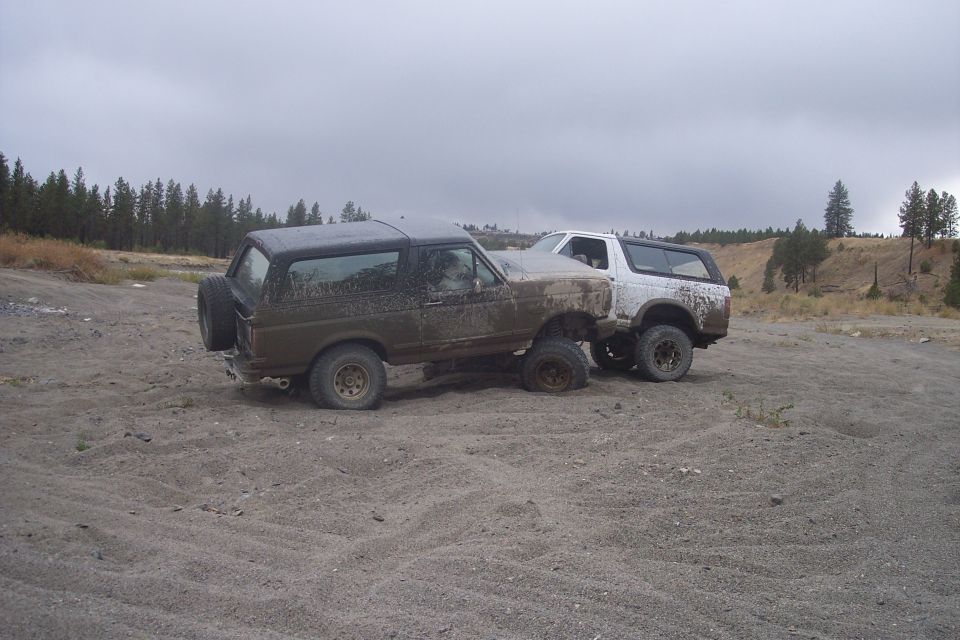 Two muddy Ford Broncos parked on a dirt lot, one behind the other
