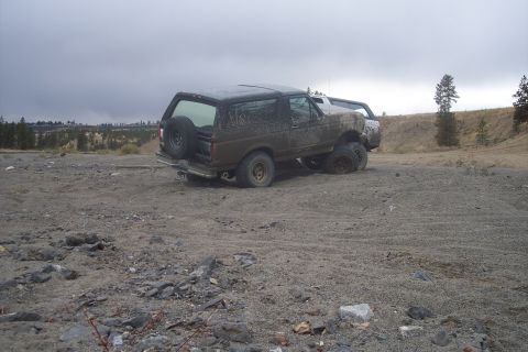 1995 Ford Bronco - A muddy Ford Bronco is stuck in a dirt lot with another vehicle behind it.