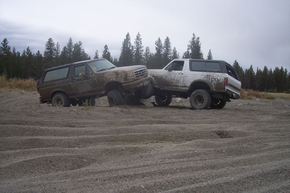 Two muddy 1995 Ford Broncos stuck in sand, one with its front bumper against the other