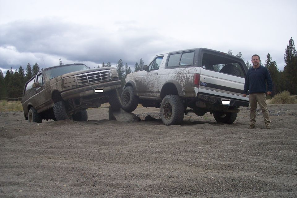 Two Ford Broncos are off-roading on a dirt path with a man standing next to one of them