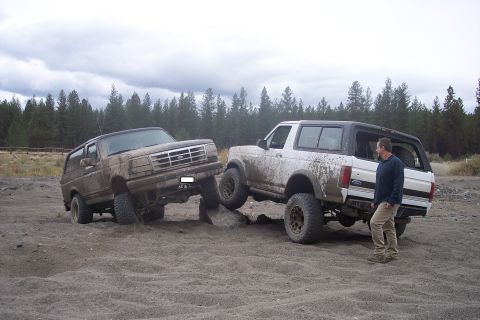1995 Ford Bronco - Two Ford Broncos navigate a challenging off-road course, one with a man observing the action.