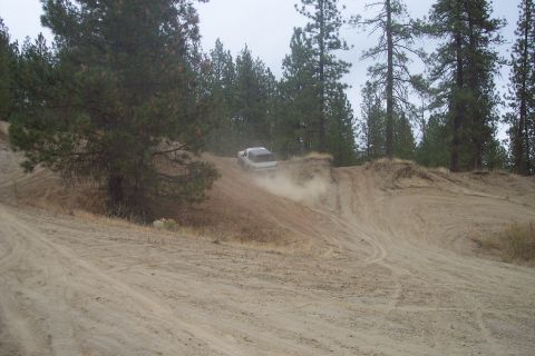 1995 Ford Bronco - A white SUV navigates a dusty, off-road trail surrounded by pine trees.